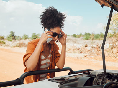Woman in an orange top on the phone looking under the hood of a vehicle