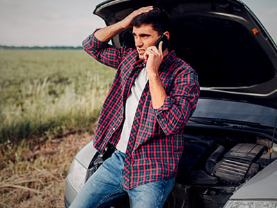 A man on the phone leaning against a car with its hood open