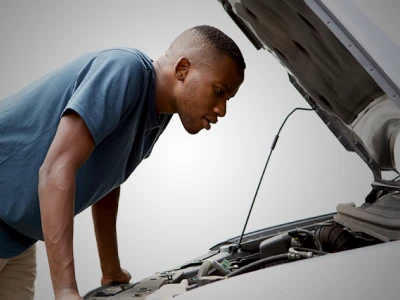 A man in a blue shirt looking at the engine of a white vehicle