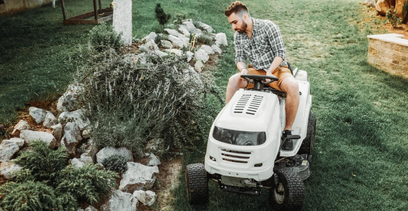 Riding a white riding lawn mower near landscaping