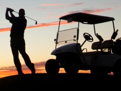 Silhouette of golfer swinging a club and a golf cart