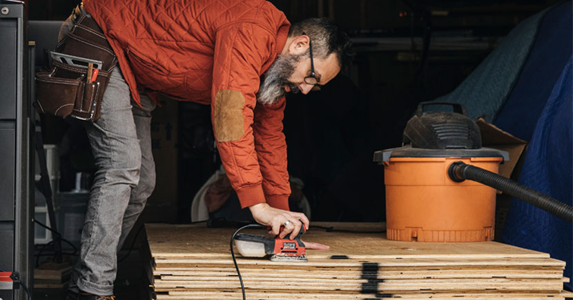 Contractor using an electric sander on some wood with a shop vac on the wood pile
