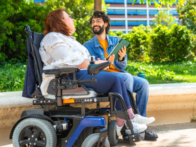 Person in an electric wheelchair talking to someone sitting on a bench
