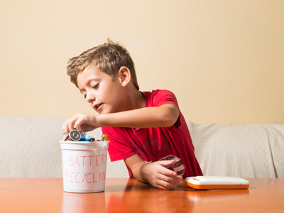 Little boy looking in a bucket of batteries for recycling